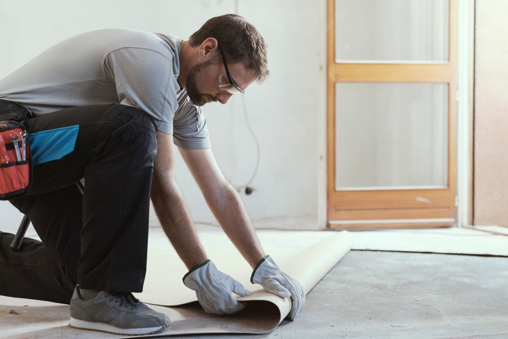 Man Kneeling, Installing Flooring. Wearing Gloves, Safety Glasses — Kalora Carpentry & Restorations in Charlestown, NSW