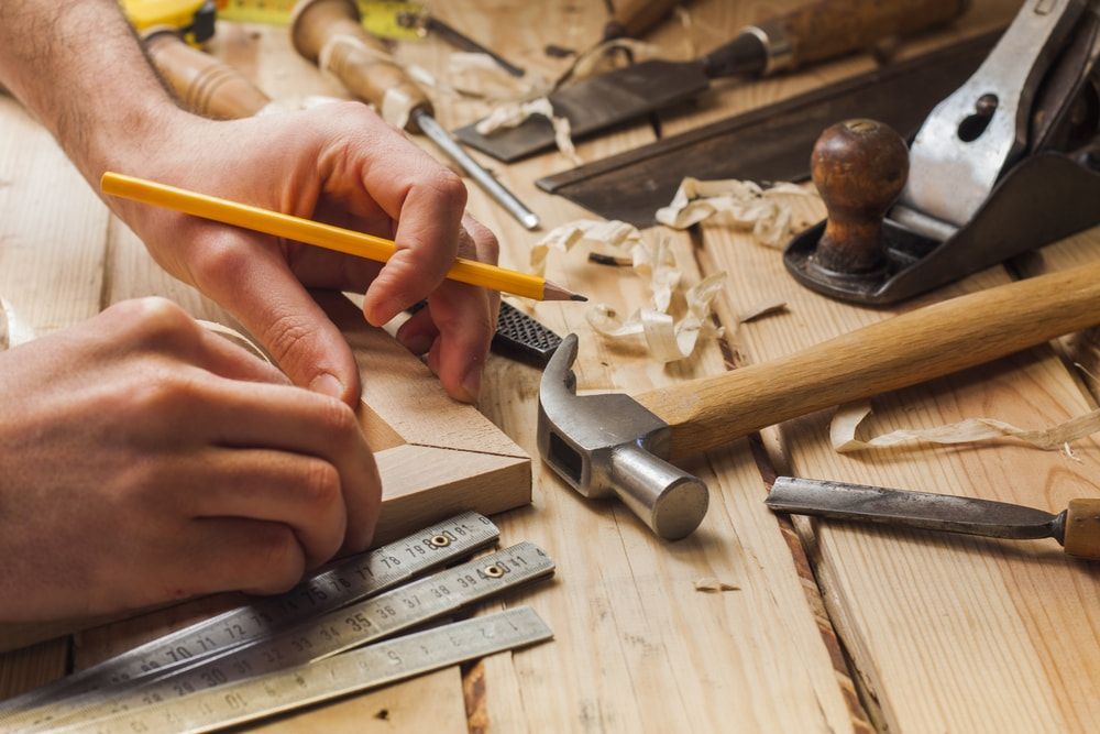 Hands Using a Pencil to Mark Wood; Carpentry Tools and Wood Shavings — Kalora Carpentry & Restorations in Charlestown, NSW