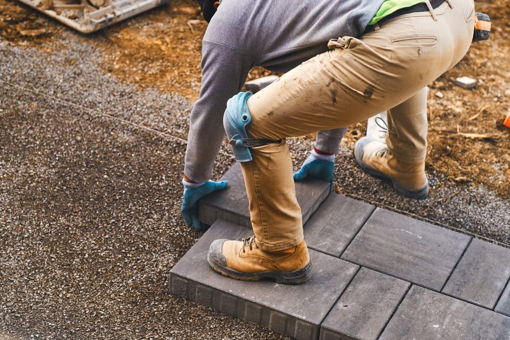 Person Laying Pavers on a Gravel Base, Wearing Work Boots and Knee Pads — Kalora Carpentry & Restorations in Charlestown, NSW