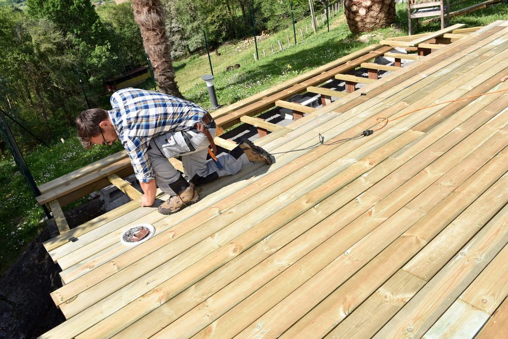 Man Building a Wooden Deck Outdoors. He's Kneeling — Kalora Carpentry & Restorations in Charlestown, NSW