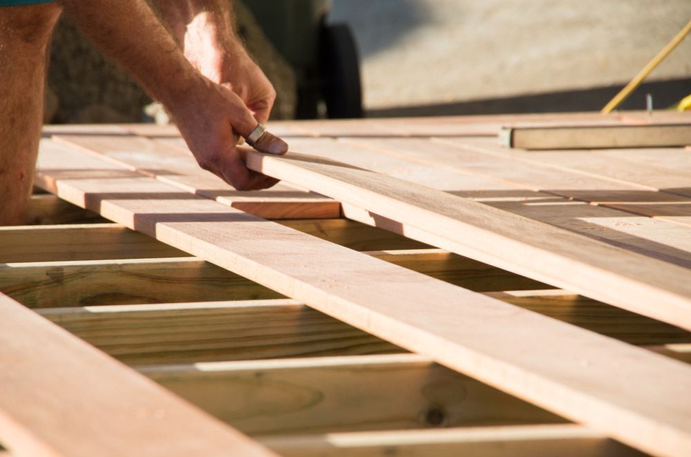 Person Building a Wooden Deck; Hands Placing a Plank Onto the Frame — Kalora Carpentry & Restorations in Charlestown, NSW