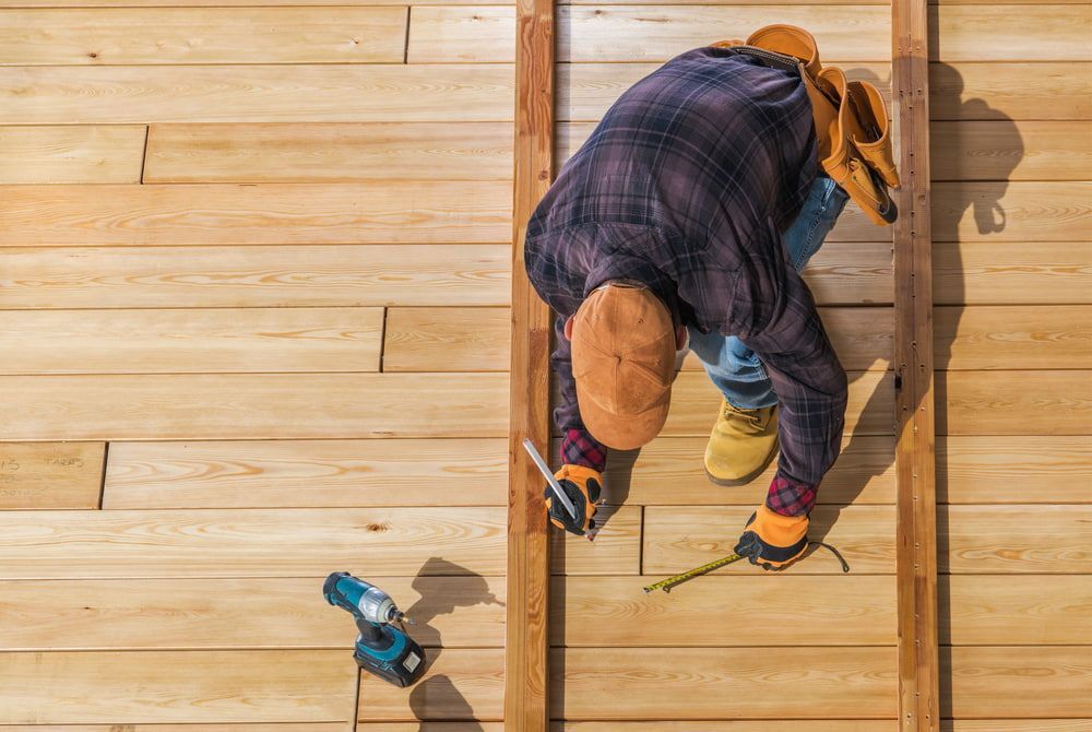 Carpenter in Plaid Shirt, Using a Level on Wooden Deck — Kalora Carpentry & Restorations in Charlestown, NSW