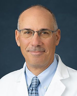A man in a white coat and tie is smiling for the camera.