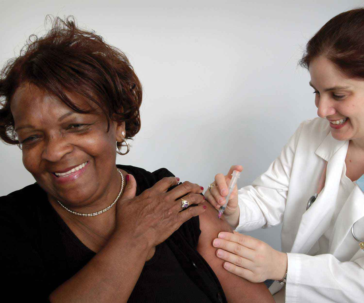 Woman receiving a shoulder injection from a clinician, smiling during the vaccination.