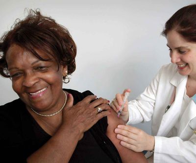 Woman receiving a shoulder injection from a clinician, smiling during the vaccination.