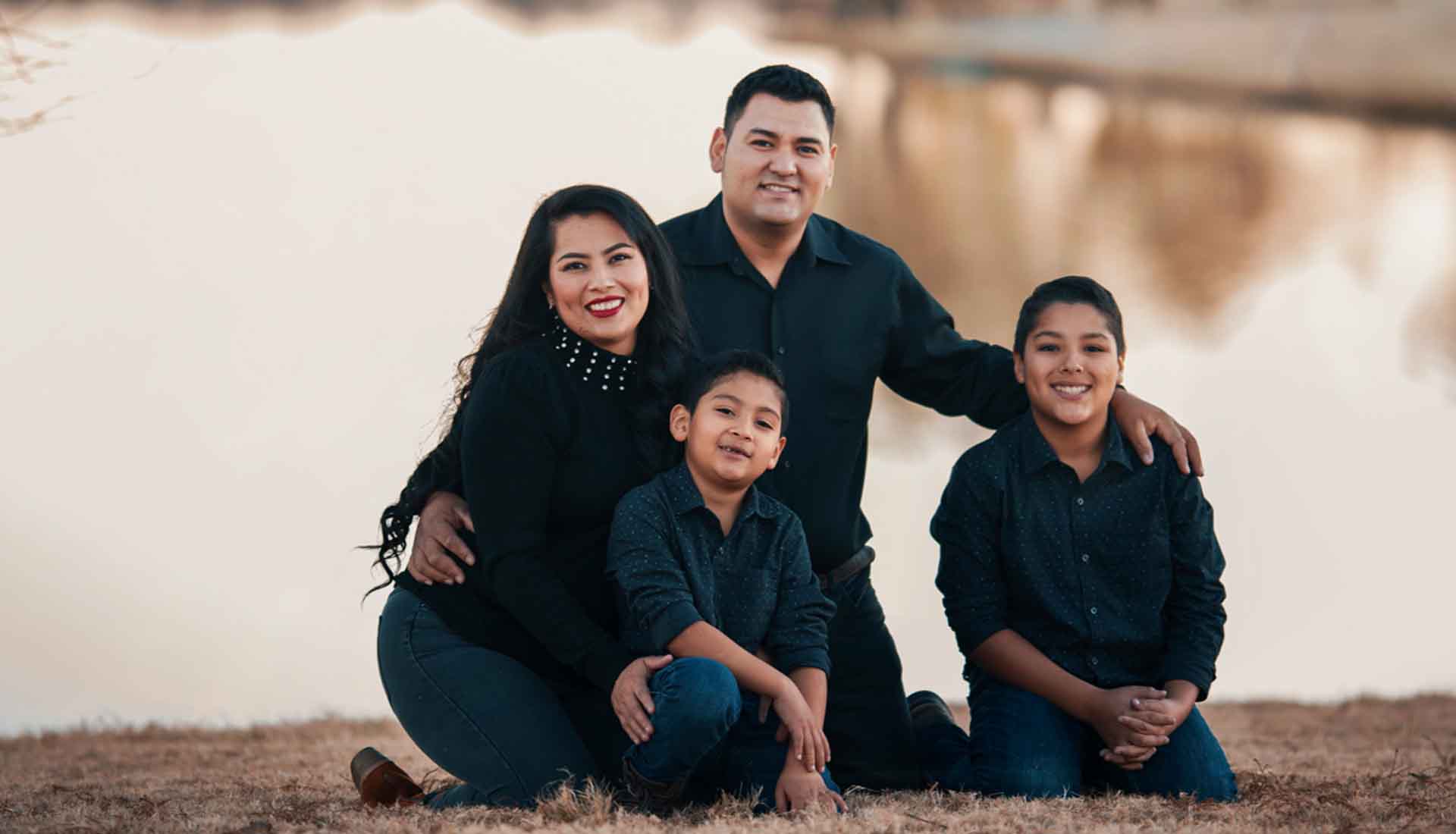 Family of four posing outdoors on a dirt path, all wearing black and smiling at the camera.