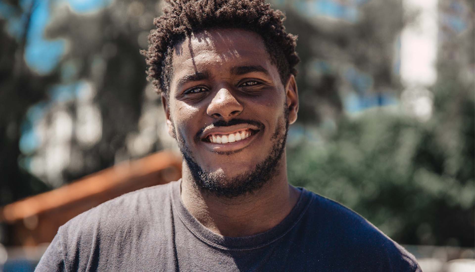 Smiling person in a dark T-shirt outdoors with a blurred background