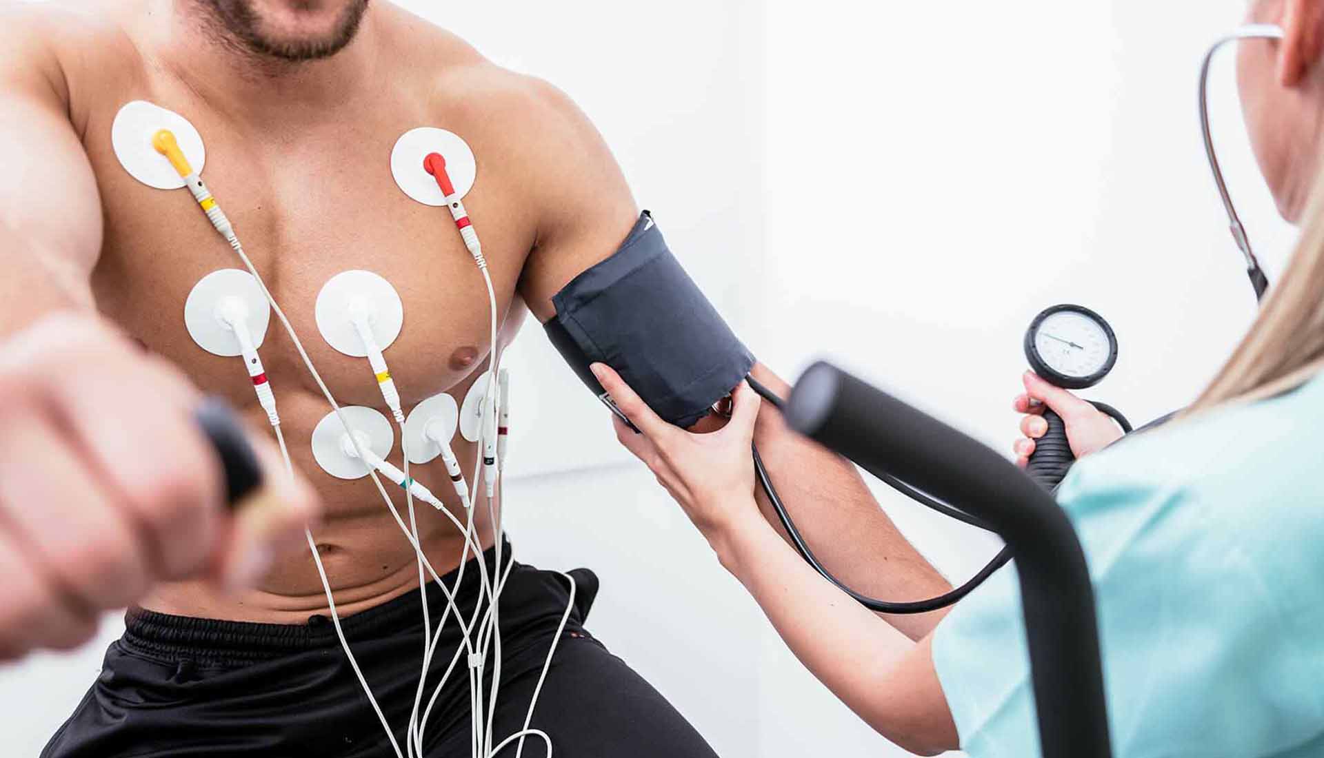 Person in medical exam with ECG electrodes on chest and blood pressure cuff being checked by clinician