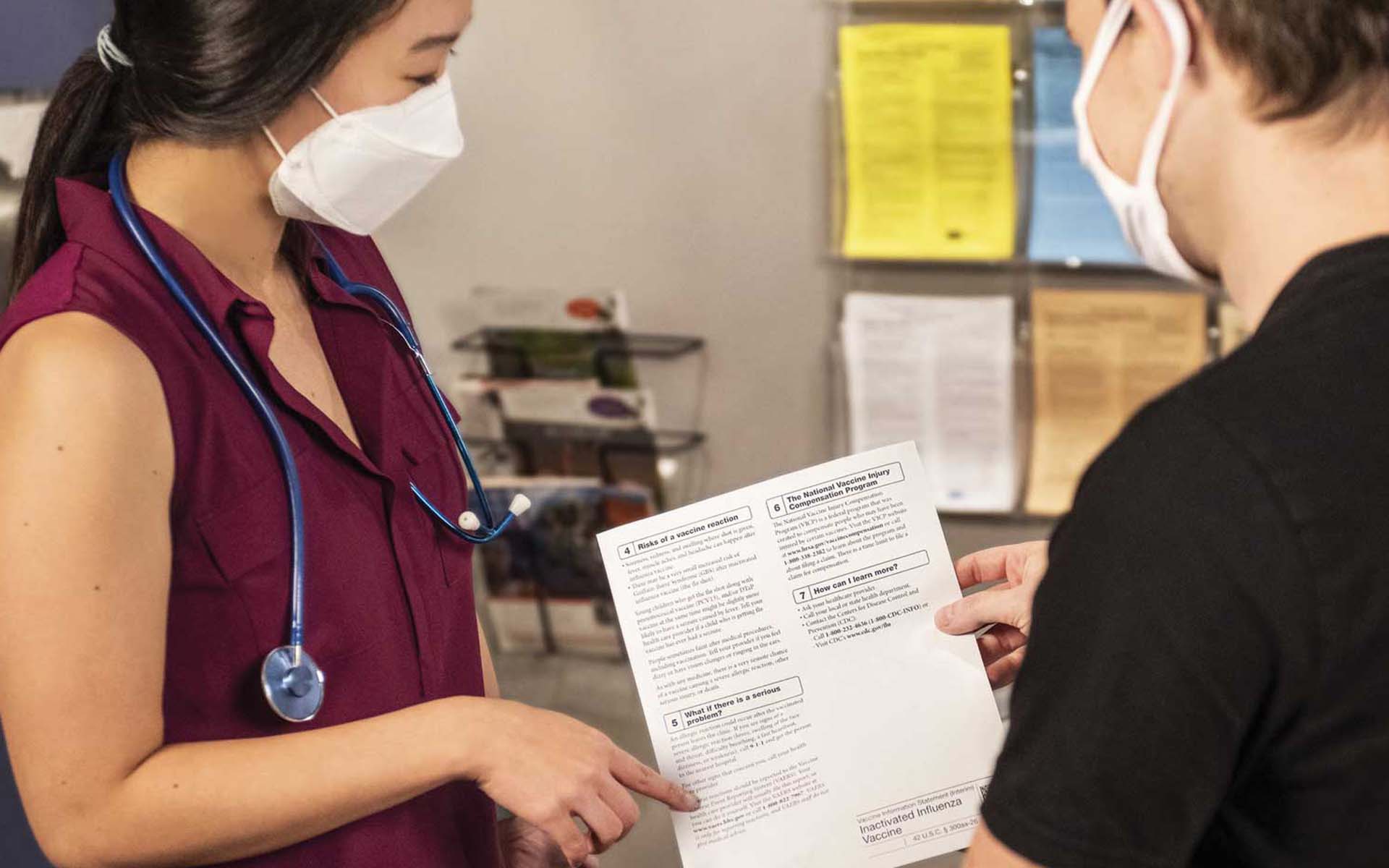 Healthcare worker discussing a document with a patient in a clinic hallway