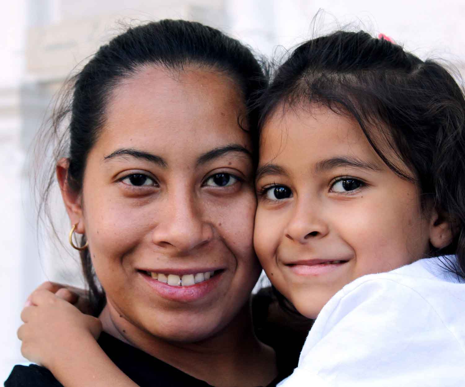 Smiling adult and child close together, faces touching, in a bright outdoor setting