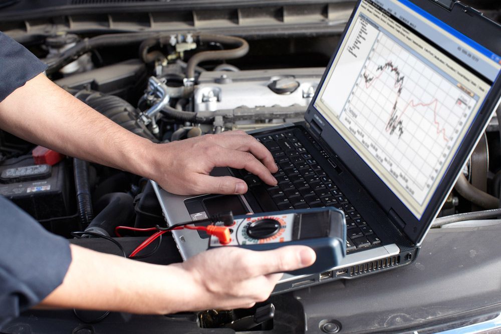 A Man Is Using A Laptop Computer Under The Hood Of A Car — Crossway Wreckers & Mechanical In Cairns, QLD