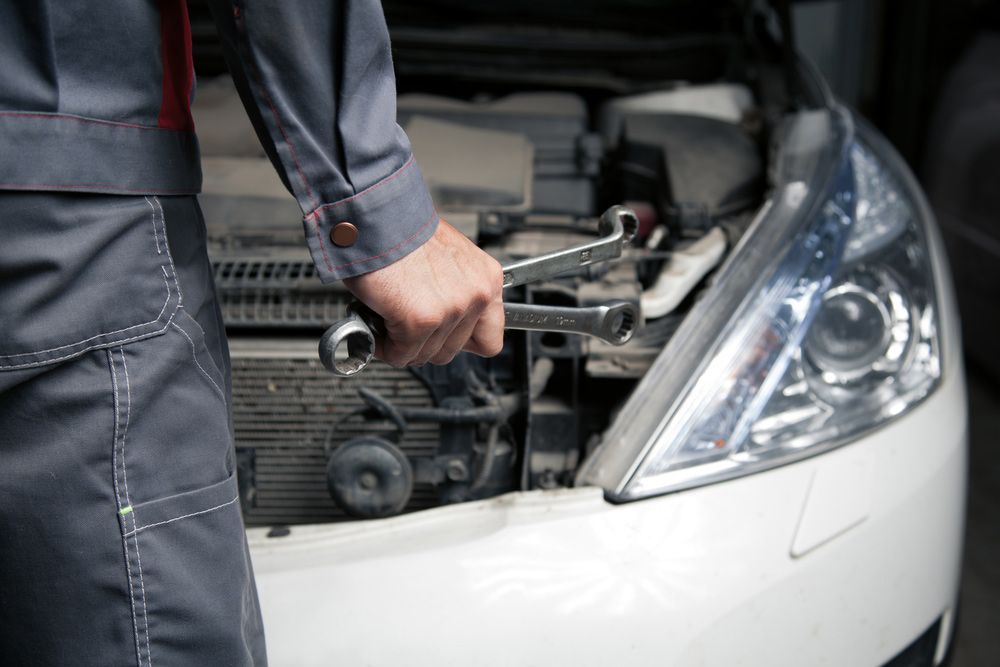 A Mechanic Is Holding A Wrench In Front Of A Car With The Hood Open — Crossway Wreckers & Mechanical In Gordonvale, QLD