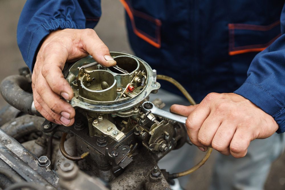 A Man Is Working On A Car Carburetor Engine With A Wrench — Crossway Wreckers & Mechanical In Gordonvale, QLD