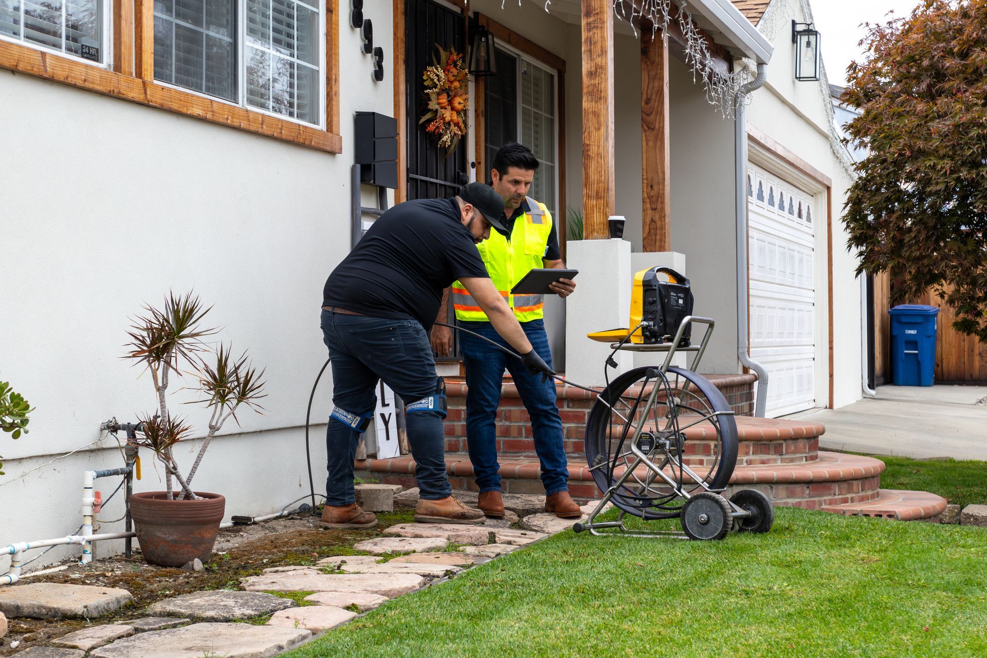 Two Monarch Plumbing workers using a tool by a house exterior