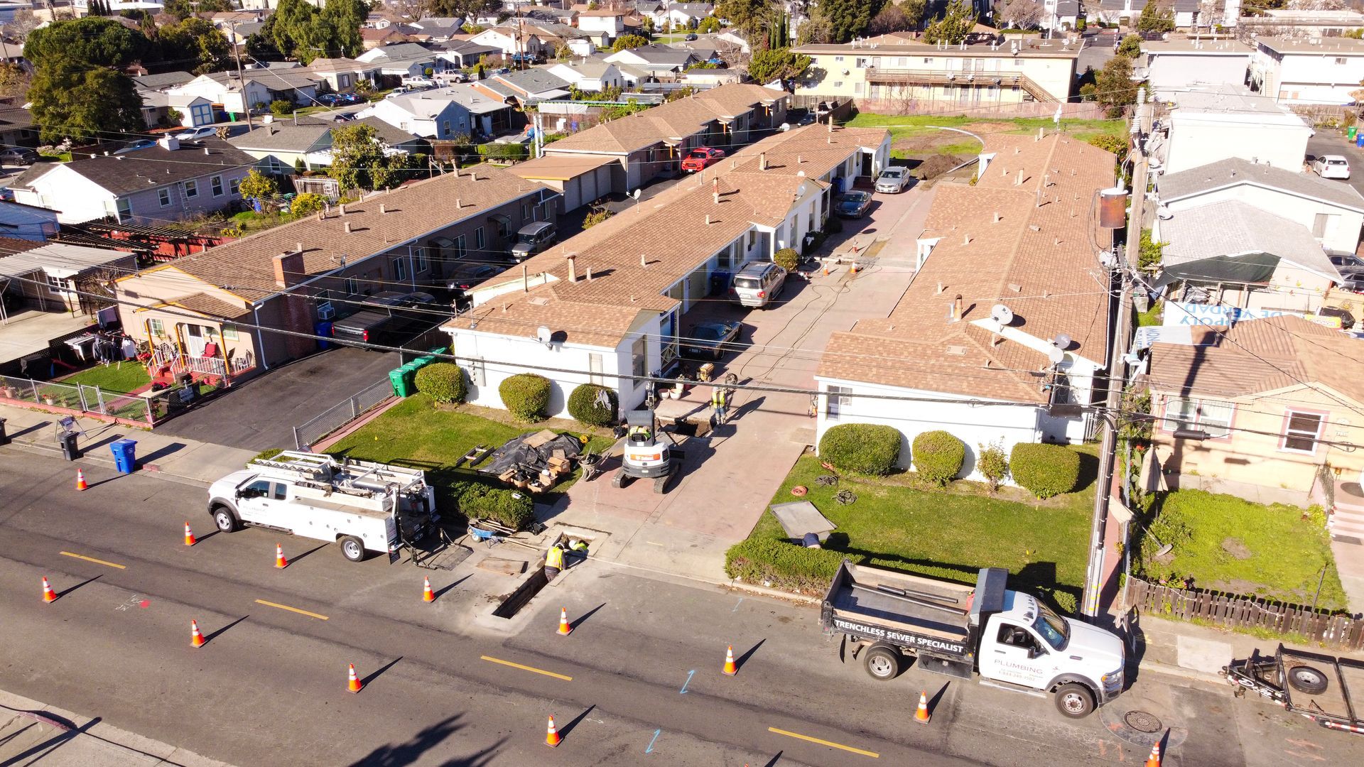 Aerial view of a residential street with houses, parked Monarch service trucks, and plumbing work being done
