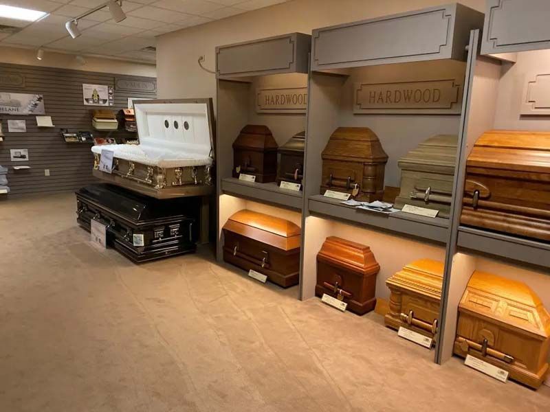 Funeral home showroom displaying various coffins, mostly brown wood.
