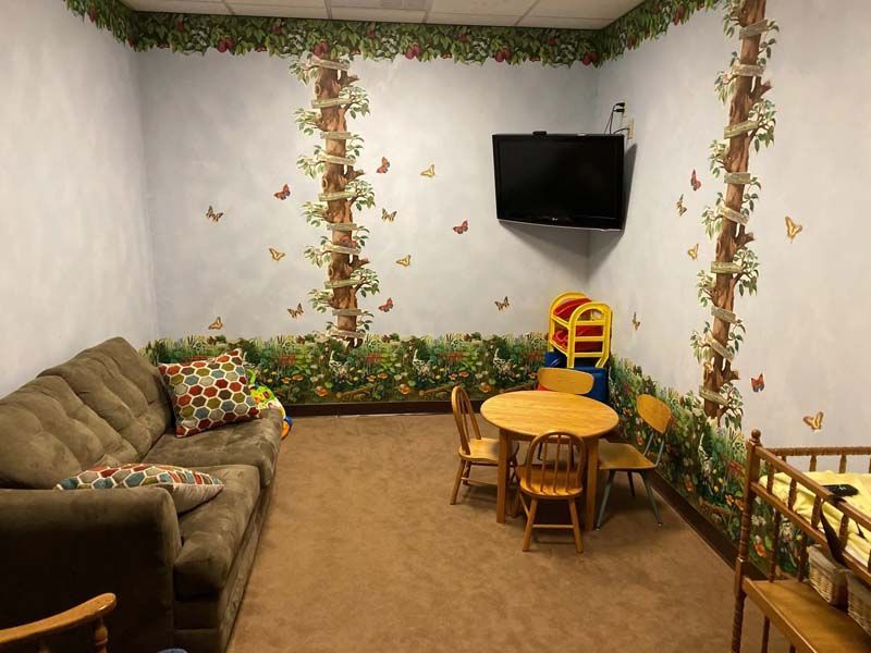A children's play area with a brown couch, a small table and chairs, a TV, and wall murals.