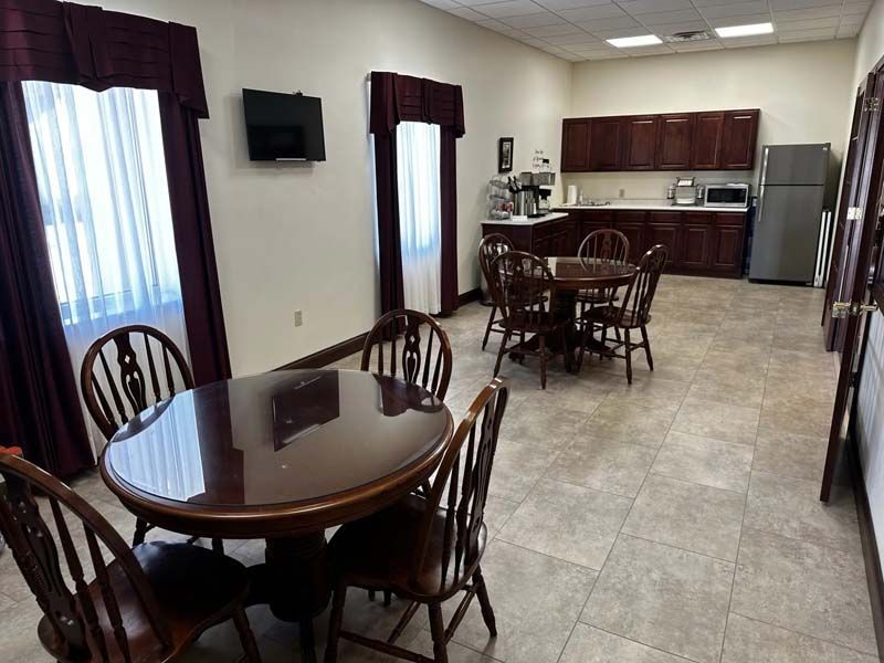A break room with two round tables, chairs, a kitchenette, windows, and a refrigerator.