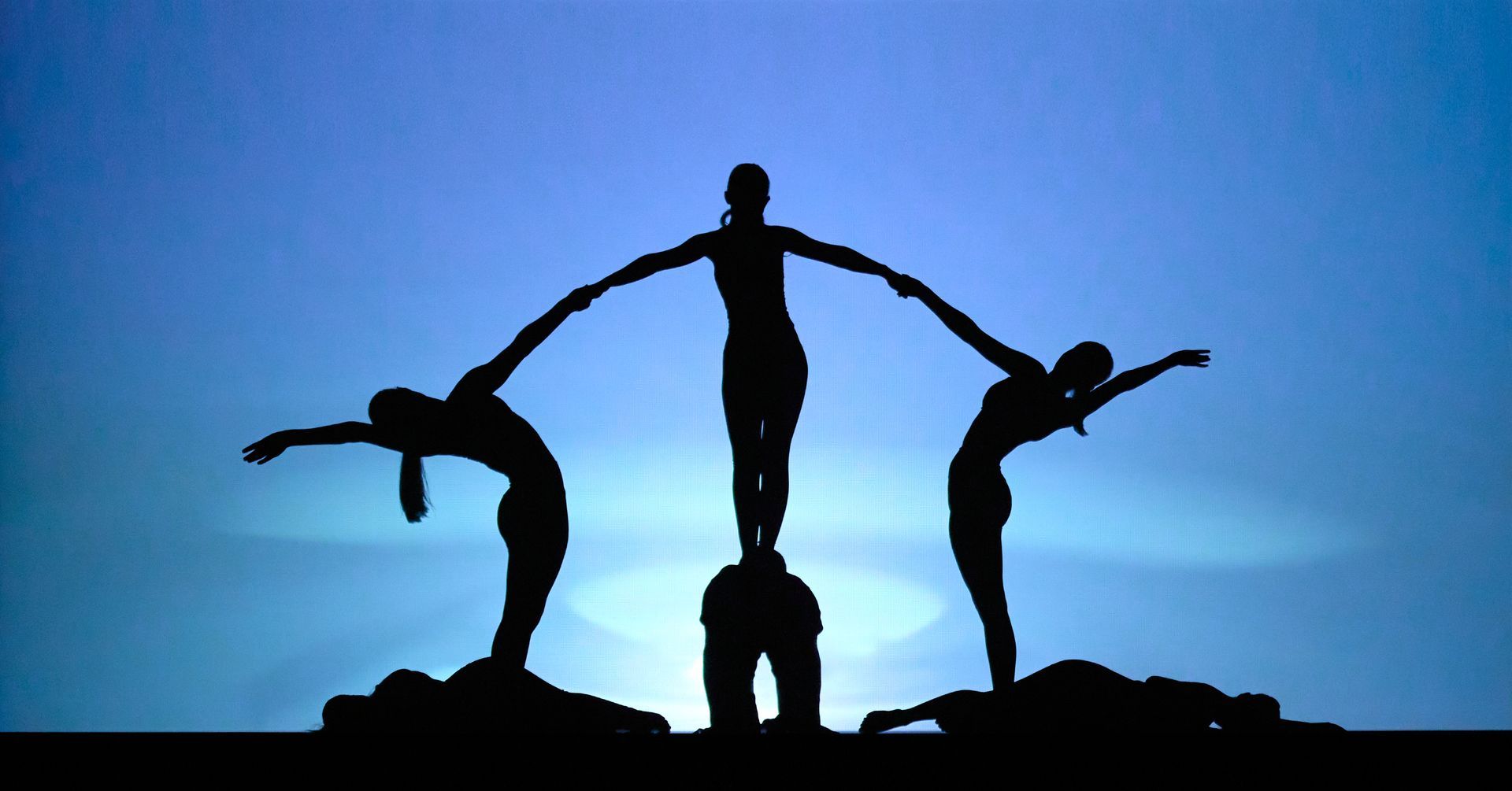 Silhouetted acrobats forming a human pyramid against a blue sunset sky