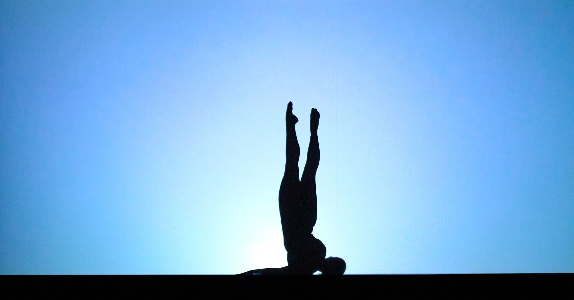 Silhouette of a person balancing upside down against a bright blue sky