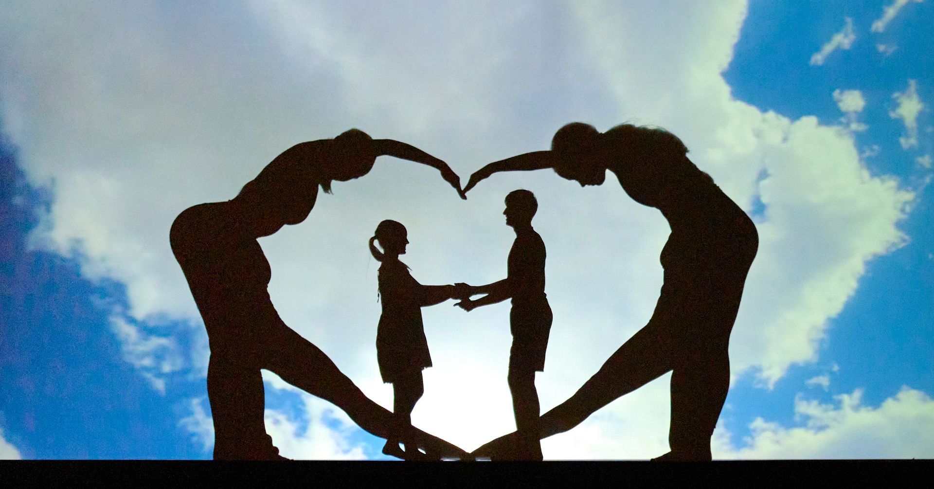 Silhouettes of two adults forming a heart shape around a child against a bright blue sky
