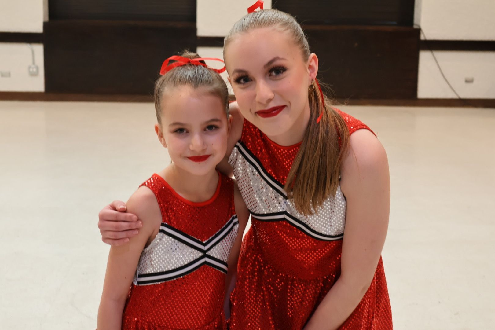 Two gymnasts in red leotards pose together on a gym floor