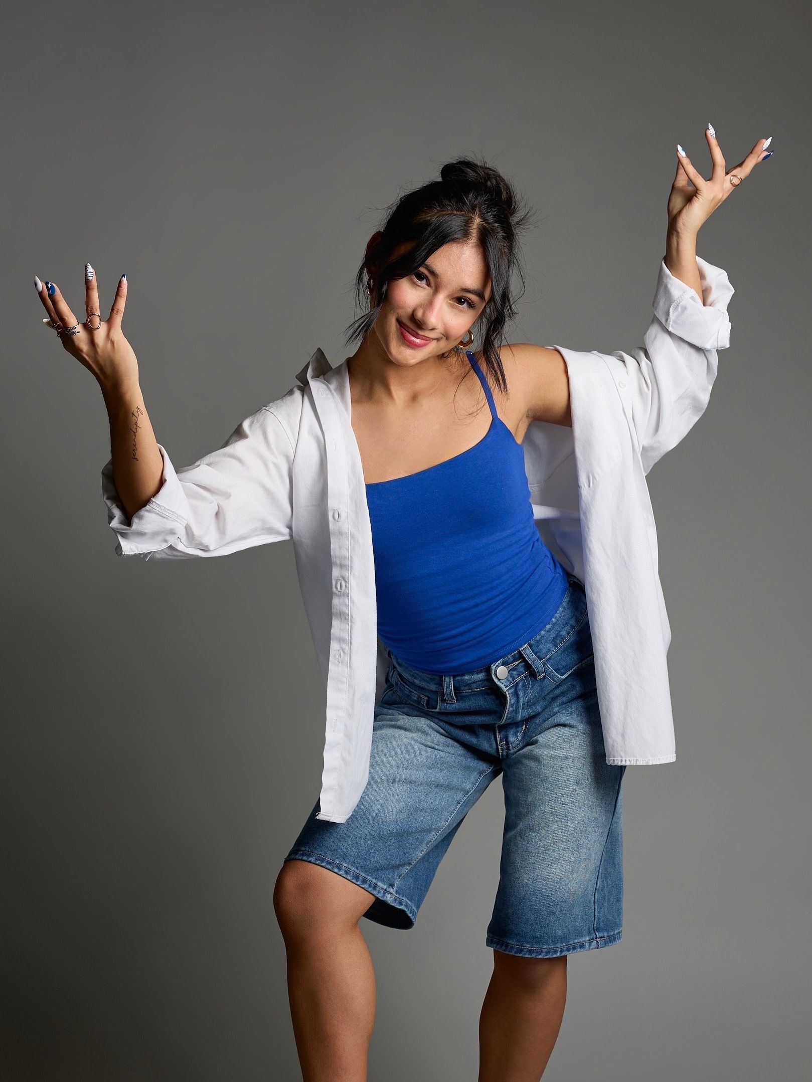Person in a black romper and smartwatch standing with hands on hips against a gray background