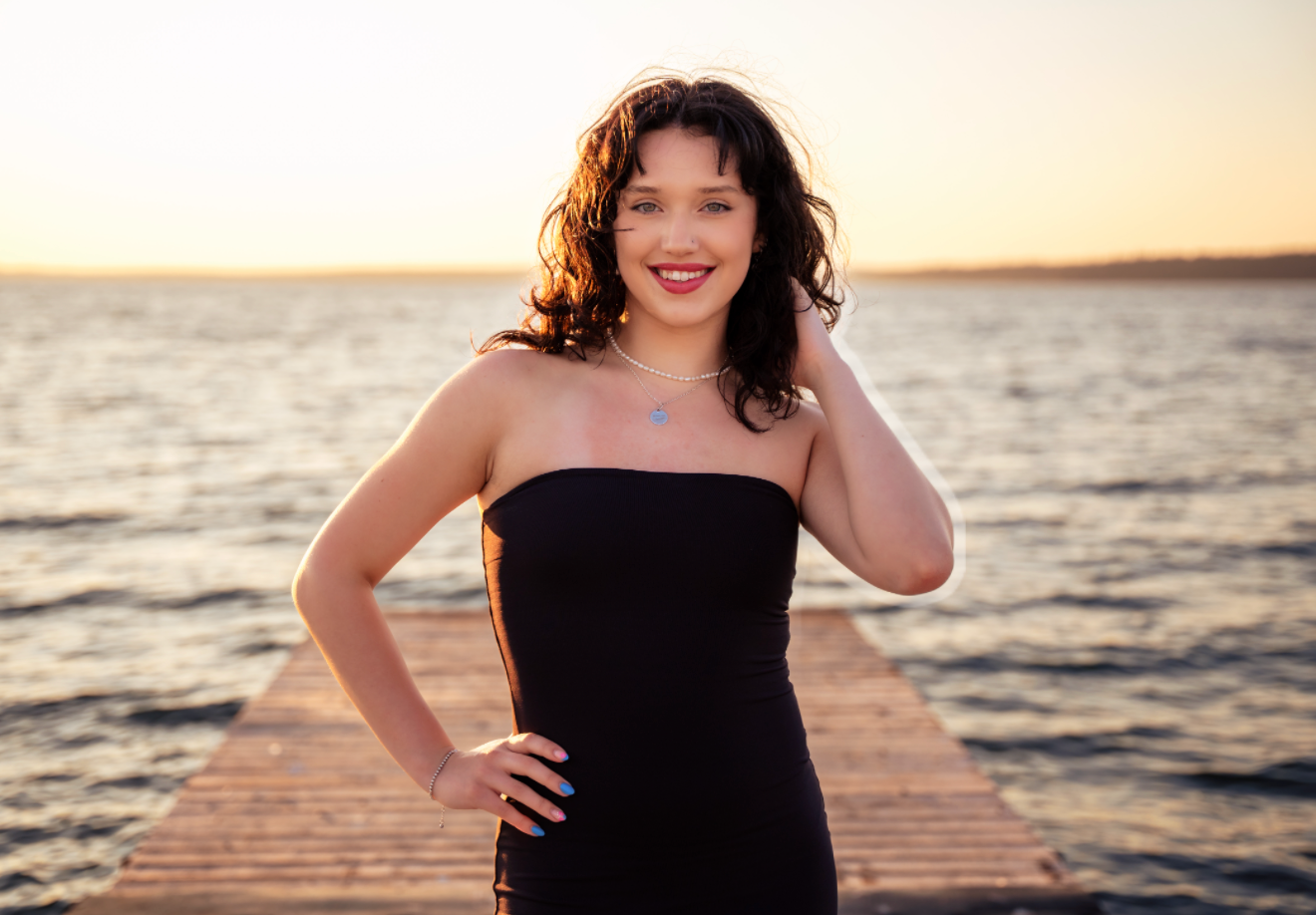 Woman standing against a white background in a black tank top, blue jeans, and black heels.