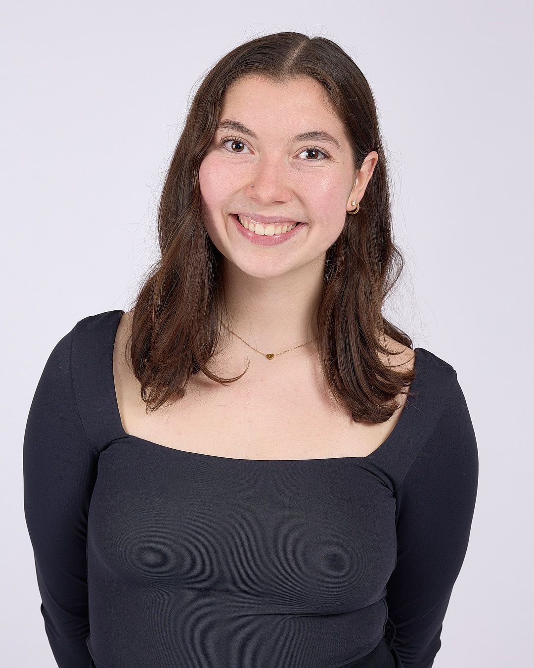 Smiling person with shoulder-length brown hair in a dark top against a light background