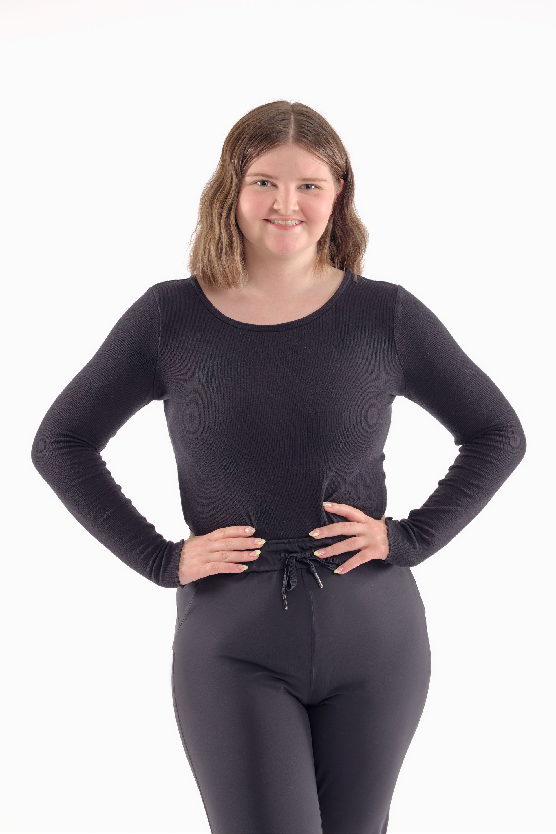 Person standing with hands on hips, wearing a black long-sleeve top and leggings on a white background.
