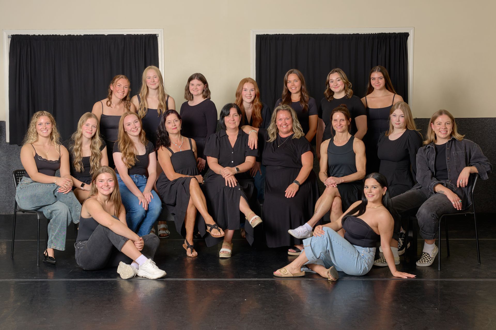 Group of people posing on a stage in black outfits with curtains behind them