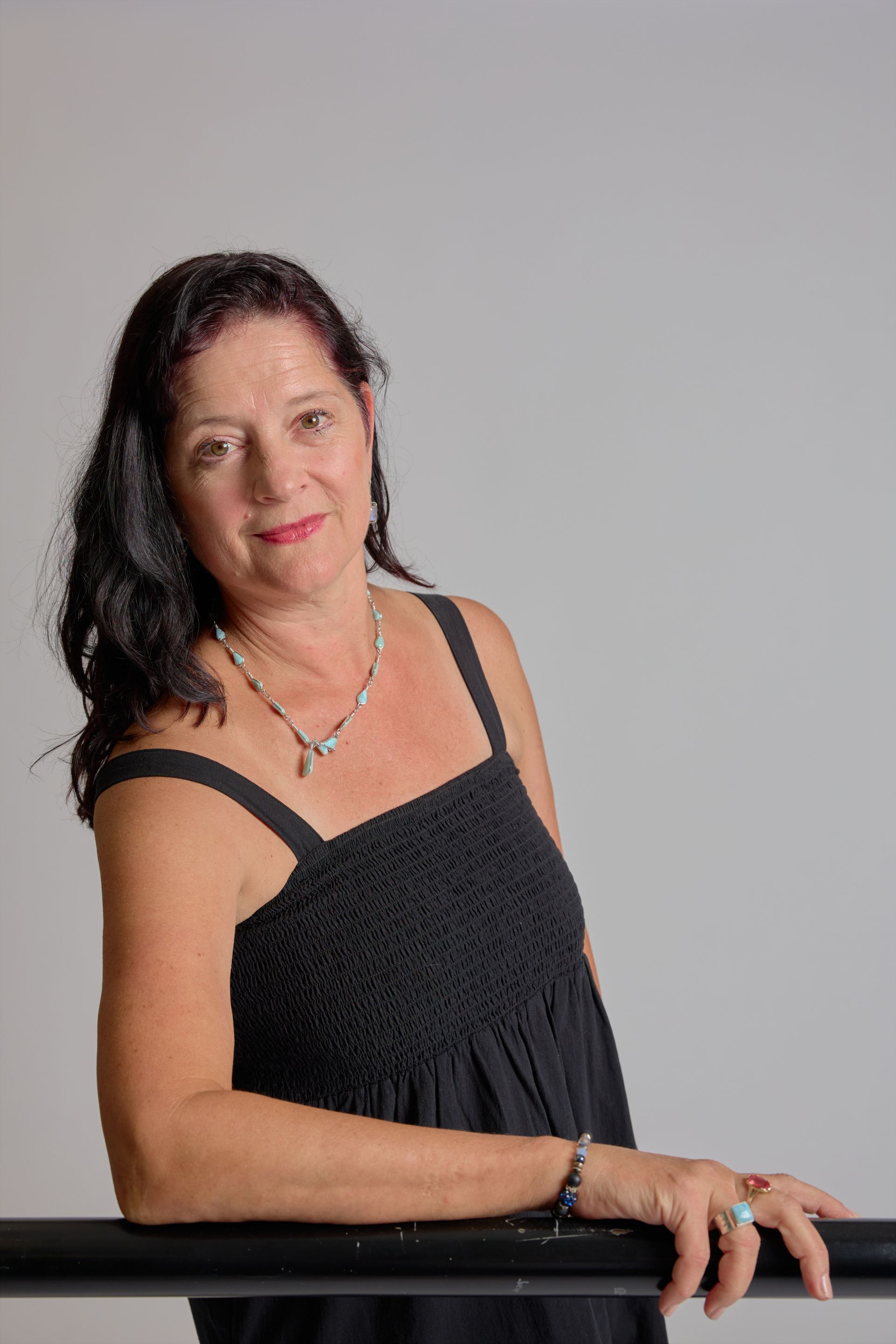 Woman in a black dress leaning on a railing against a gray background.