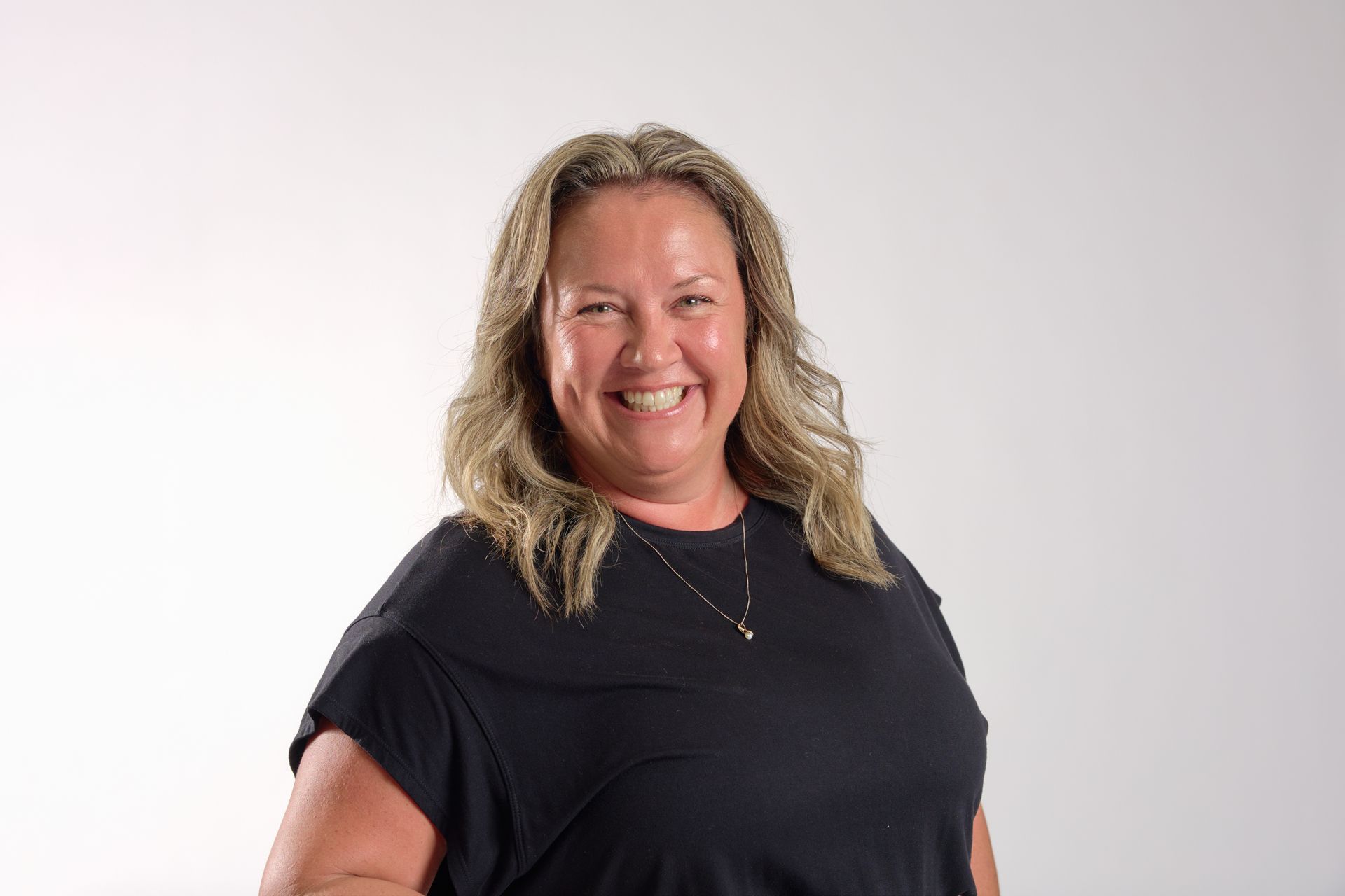 Smiling person with wavy blonde hair in a black shirt against a light background