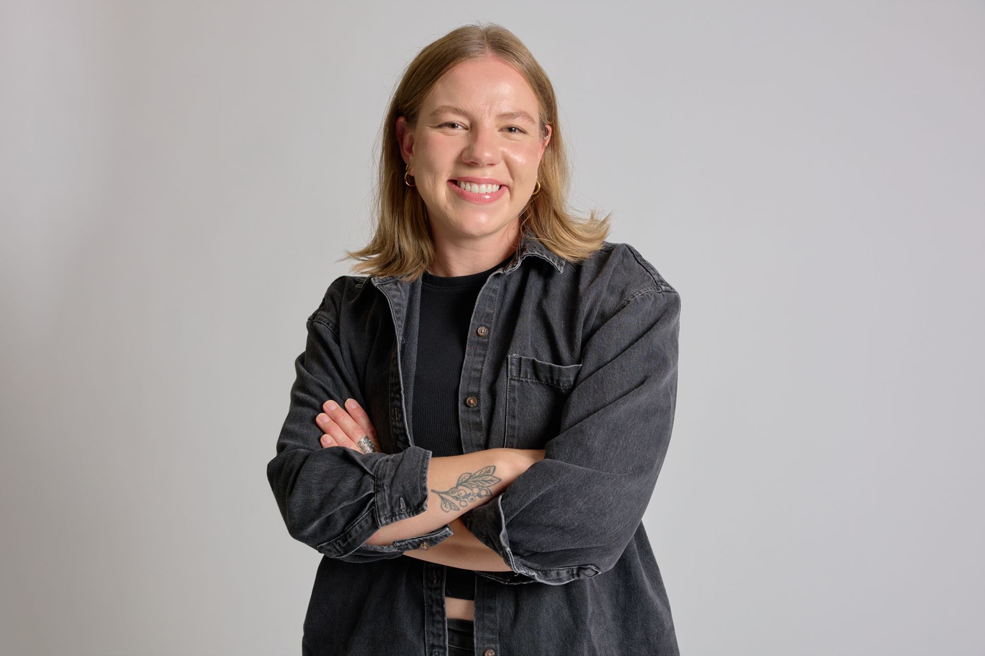 Smiling person with arms crossed, wearing a dark shirt against a light gray background
