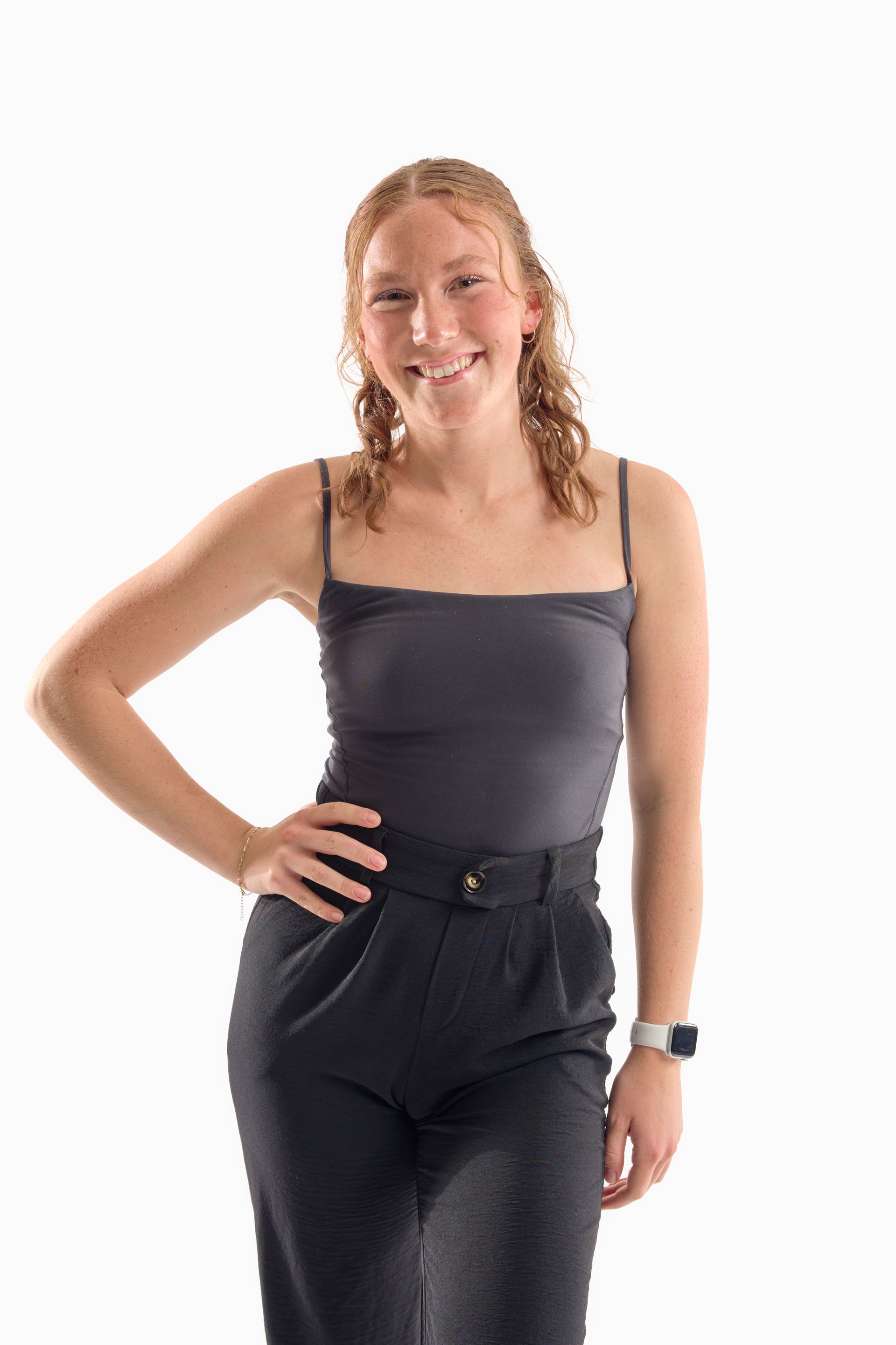 Woman standing and smiling in a gray strapless top and black pants against a white background