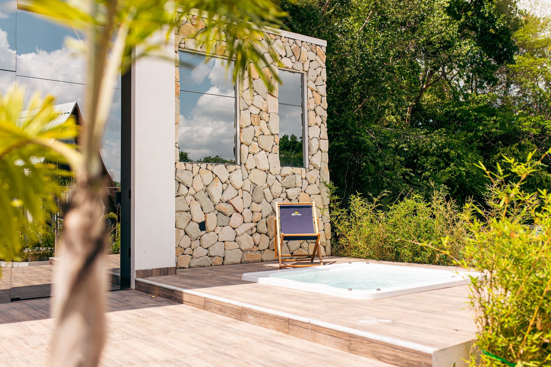 Stone-walled building with tall windows, small pool, wooden deck, and a chair, surrounded by greenery.