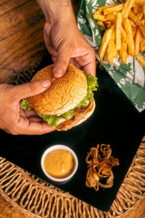 Person holding burger, with fries, sauce, and fried onions on a black surface.