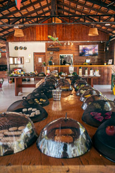 Buffet with food under dome covers on a long wooden table in a dining area.