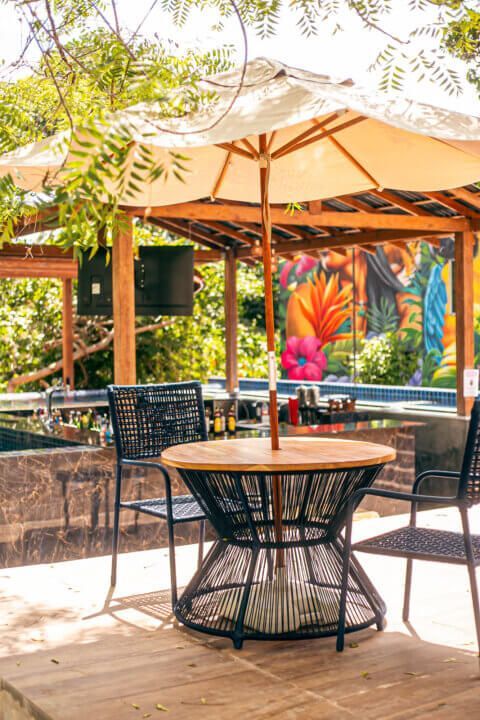 Patio dining set under a parasol, with a vibrant mural and lush greenery in the background.