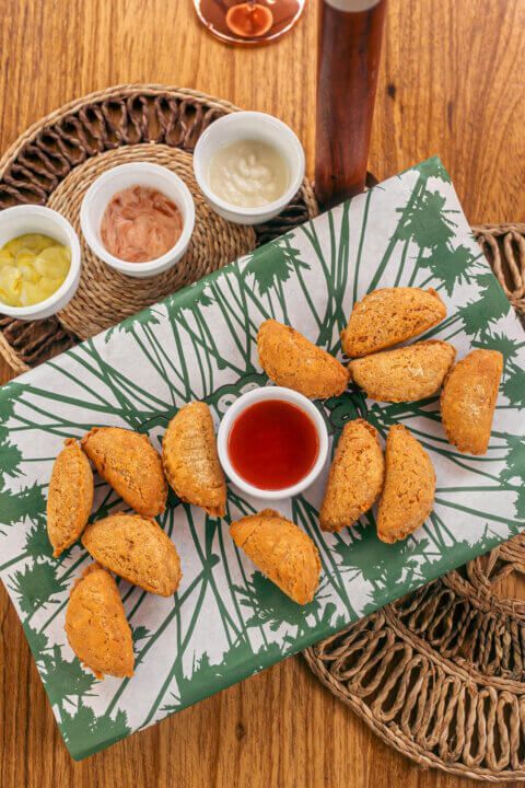 Fried savory snacks with dipping sauces on a decorated tray, with a drink on a wooden table.