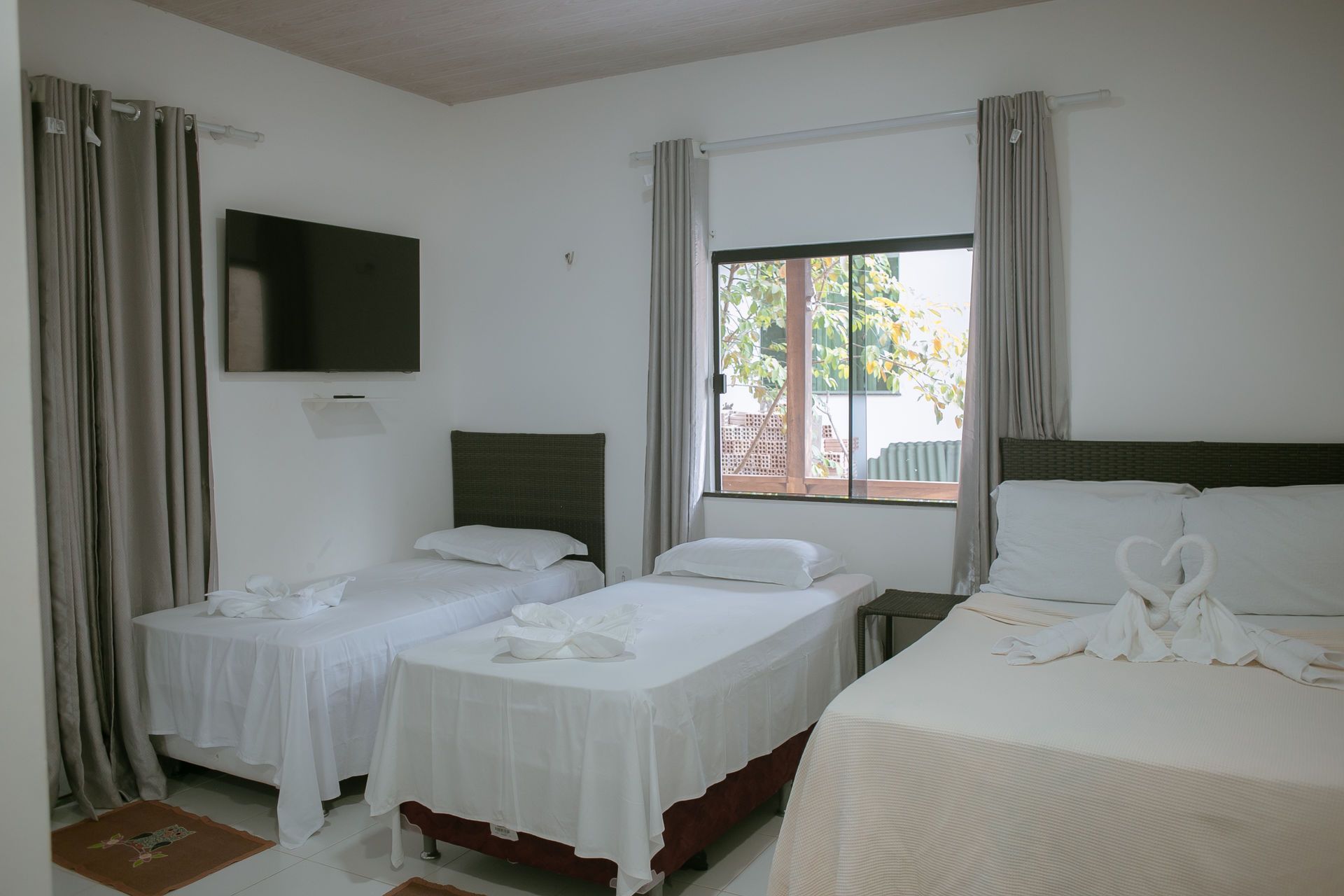 Hotel room with three beds, a TV, and a window with gray curtains.