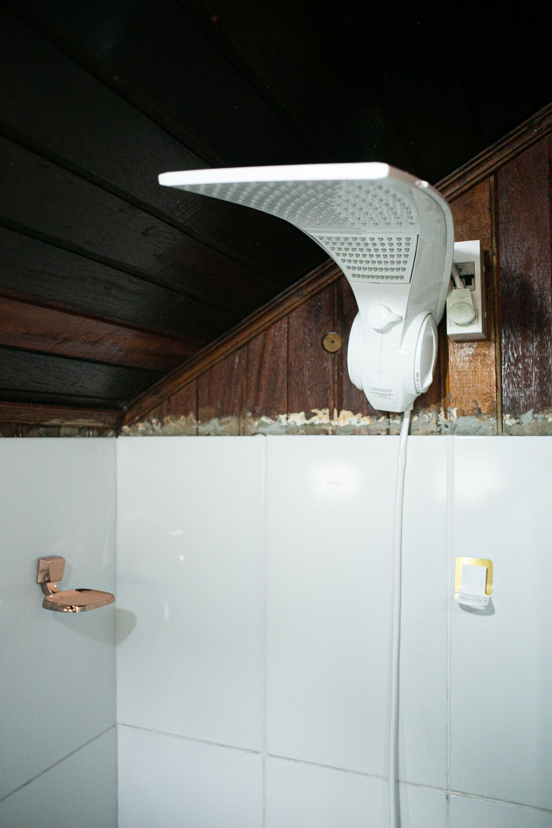 White shower head with light, mounted on a wall with a white tile surface.