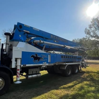 A renegade concrete pump truck is parked in a grassy field.