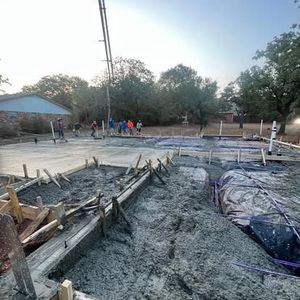 A group of people are working on a concrete base for a house.