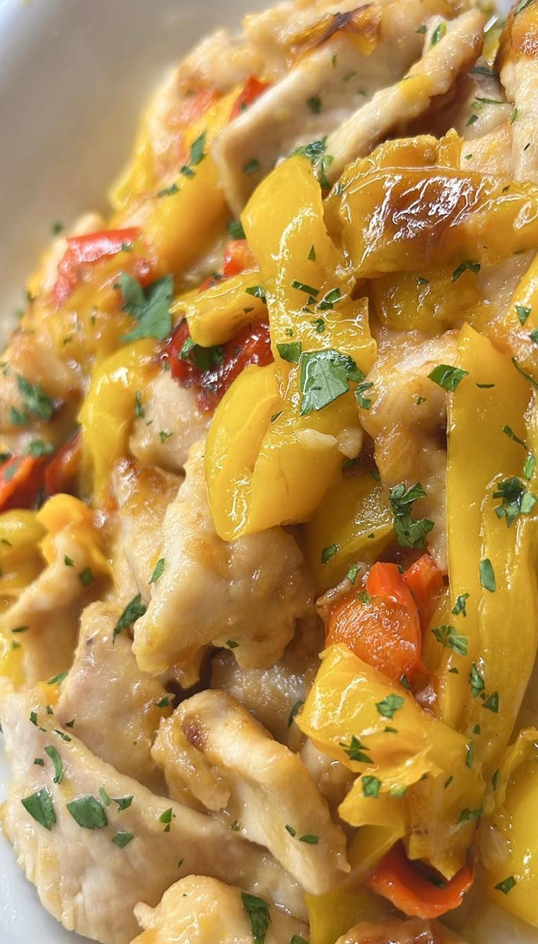 Piatto di pollo con peperoni gialli e arancioni, guarnito con prezzemolo.