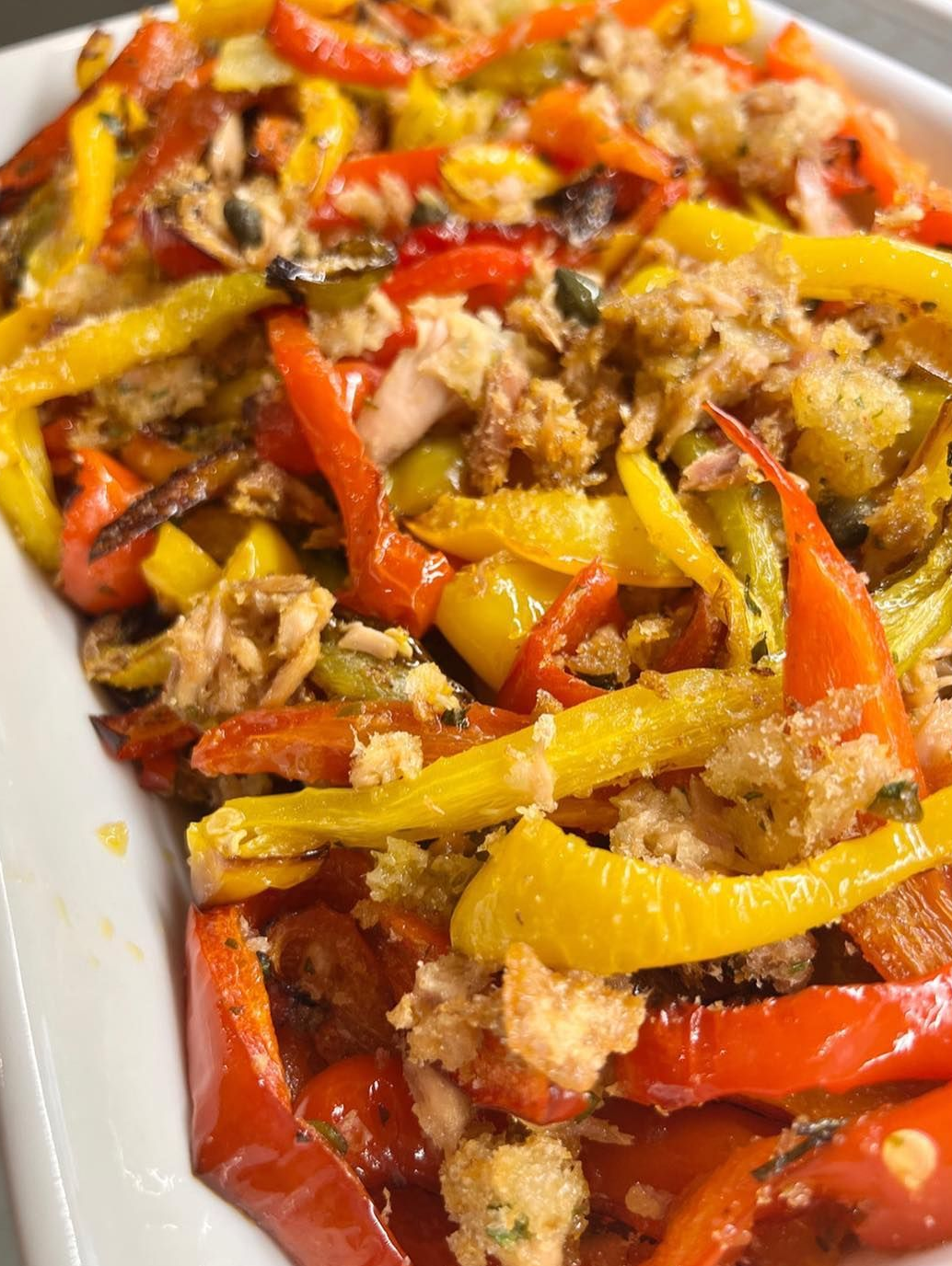 Peperoni rossi e gialli arrostiti, ricoperti di pangrattato tostato, in un piatto bianco.