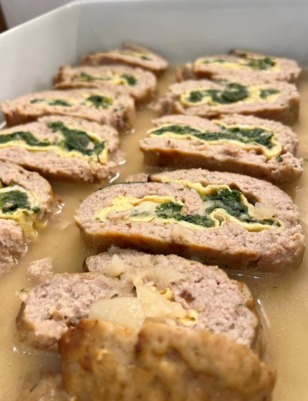Involtini di polpettone a fette, farciti con ripieno verde e strato giallo, in una salsa leggera.