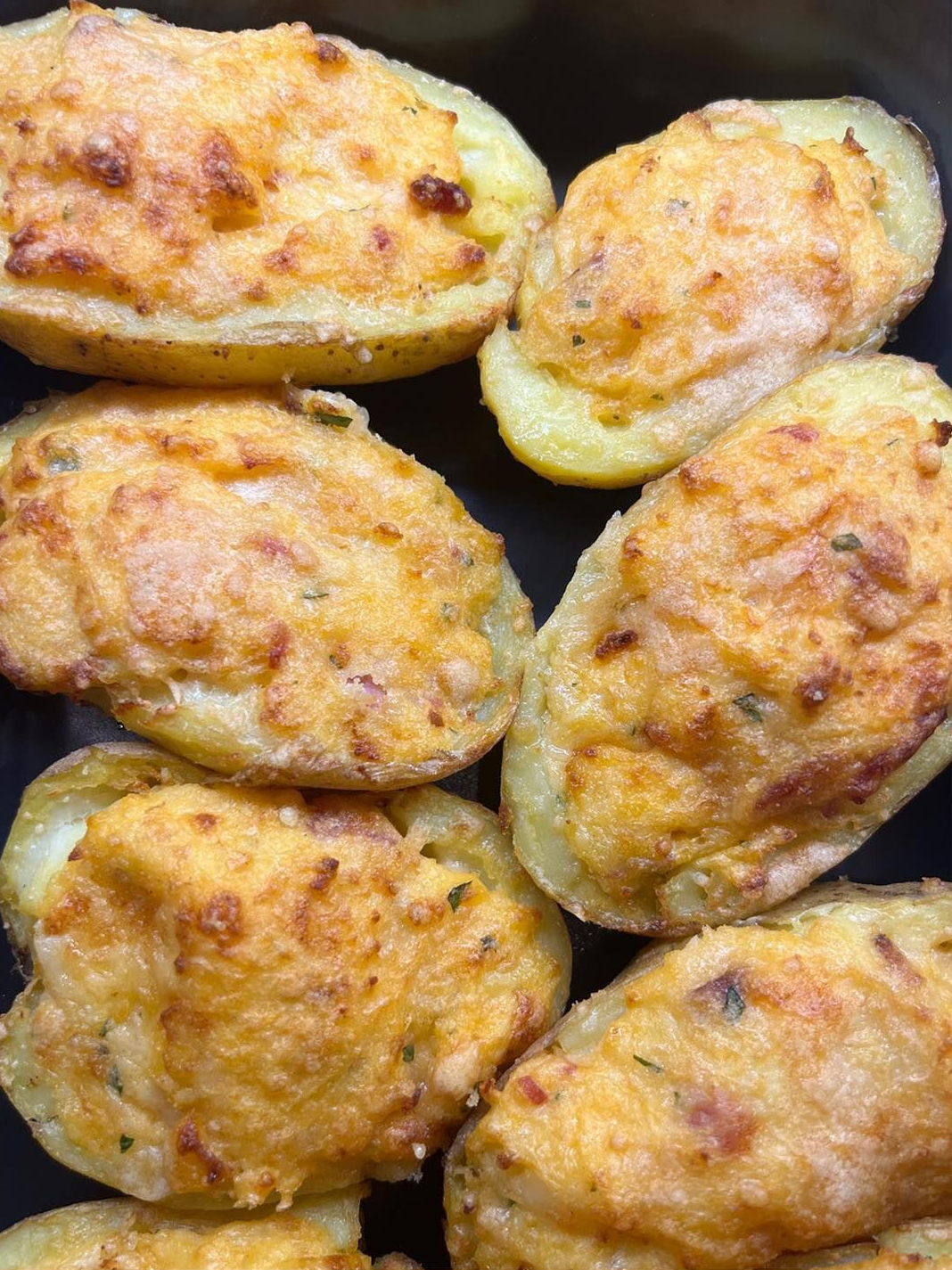Patate al forno ripiene con una copertura dorata e formaggiosa su una superficie scura.