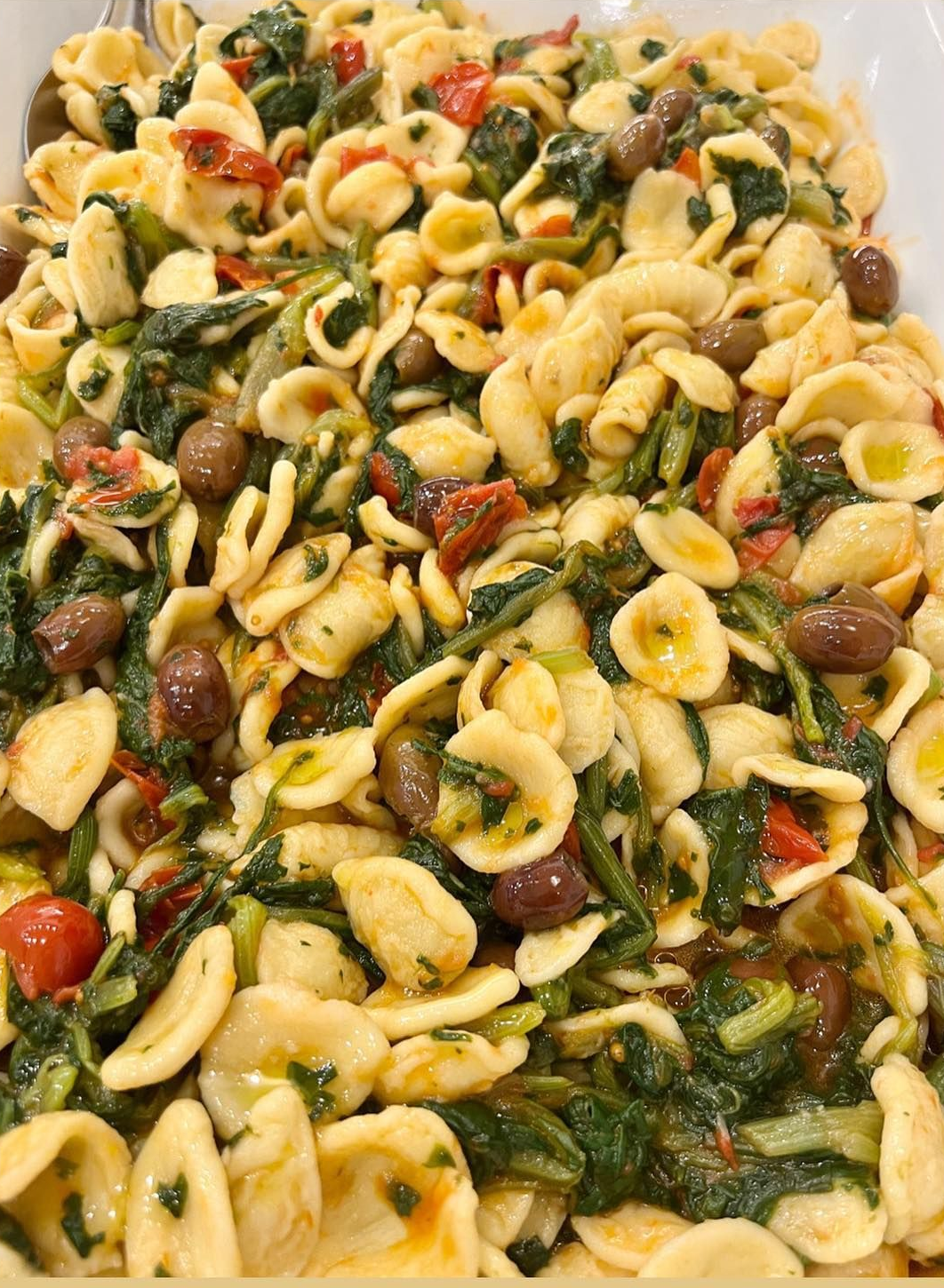 Piatto di pasta orecchiette con spinaci, pomodori e olive in una ciotola da portata.