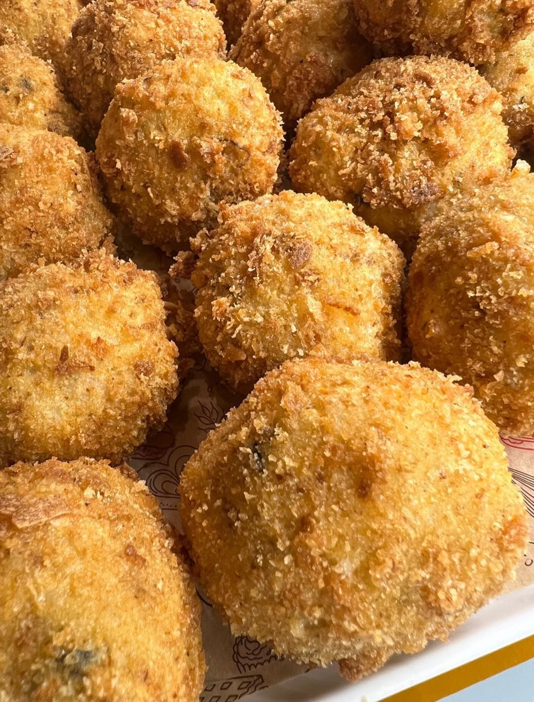 Palline di cibo dorate, fritte e impanate, forse crocchette o arancini, disposte su un vassoio.